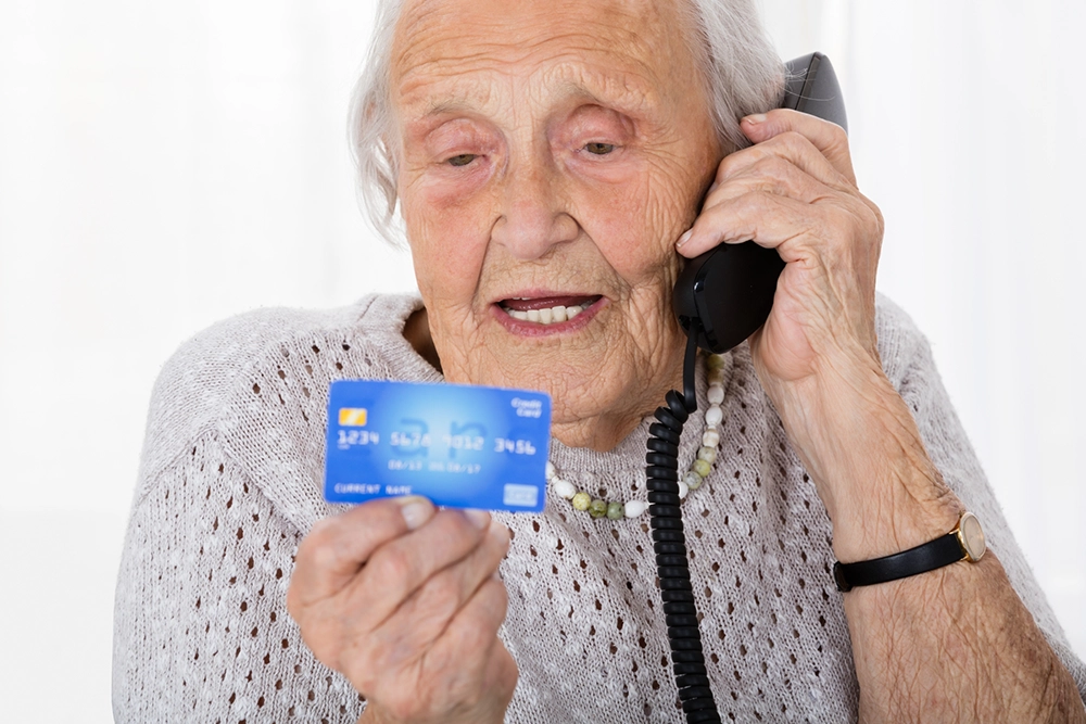 äldre kvinna pratar i telefon och hon har ett kreditkort i handen