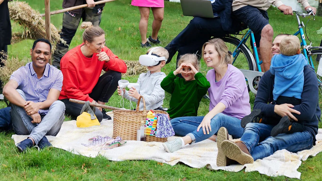 Människor i olika åldrar och härkomster sitter på en picknickfilt 