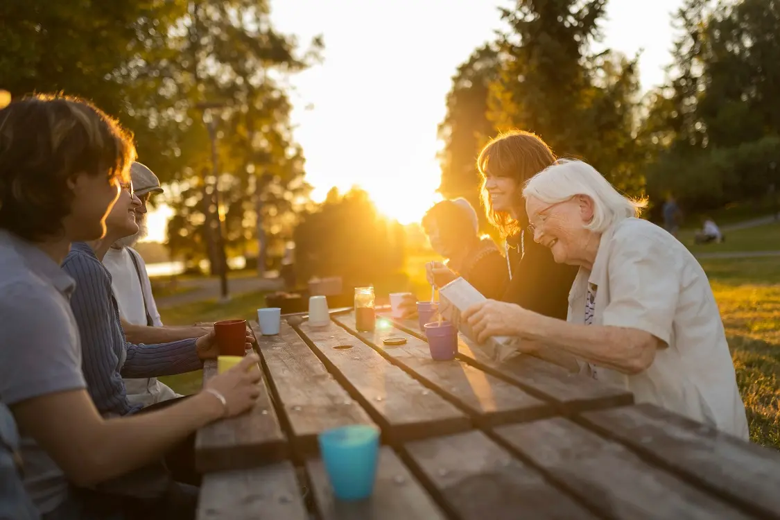 Människor i olika åldrar är samlade runt ett trädgårdsbord och fikar