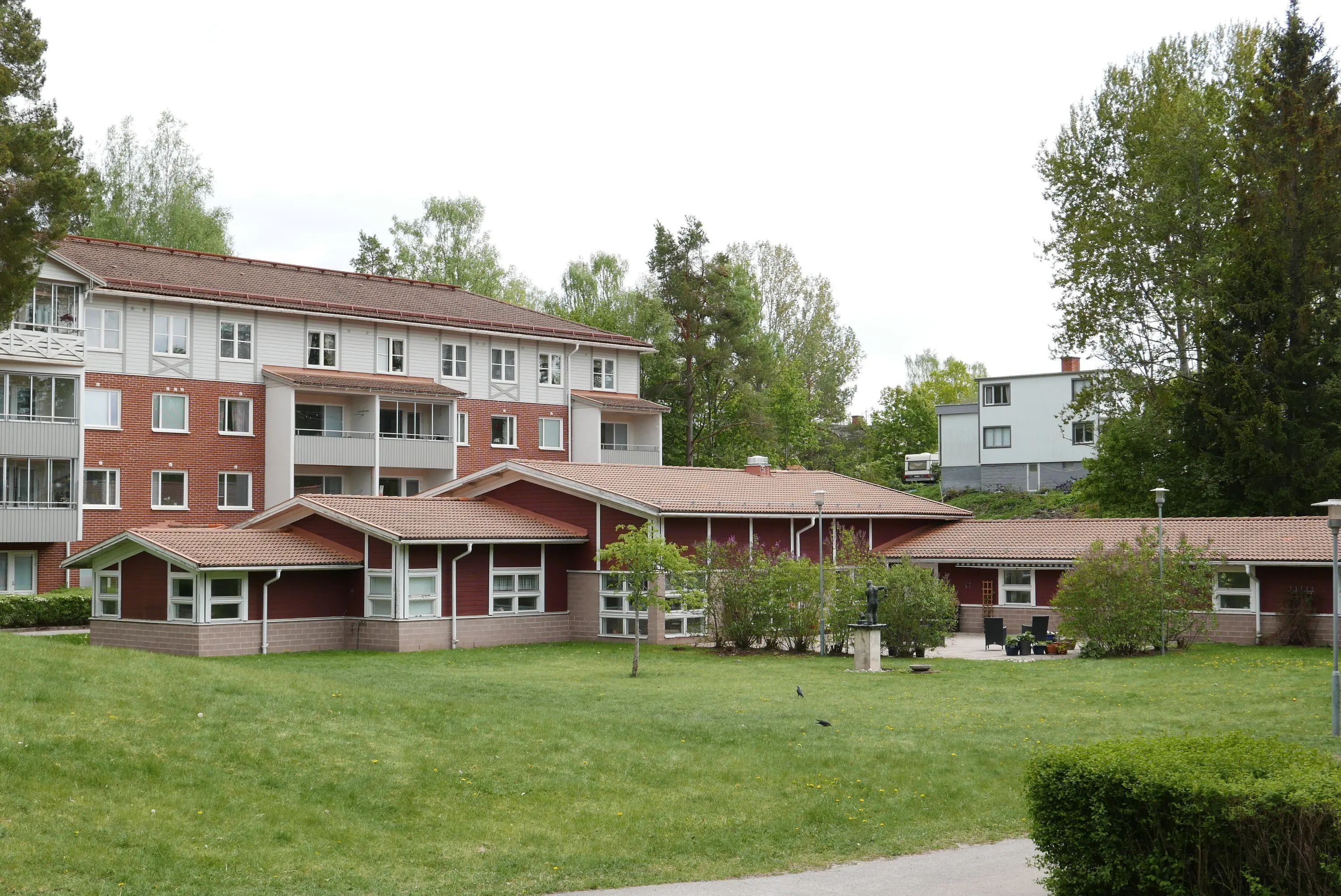 Grön gräsmatta i förgrund med ett lägenhetshus i tegel och trä i bakgrunden 