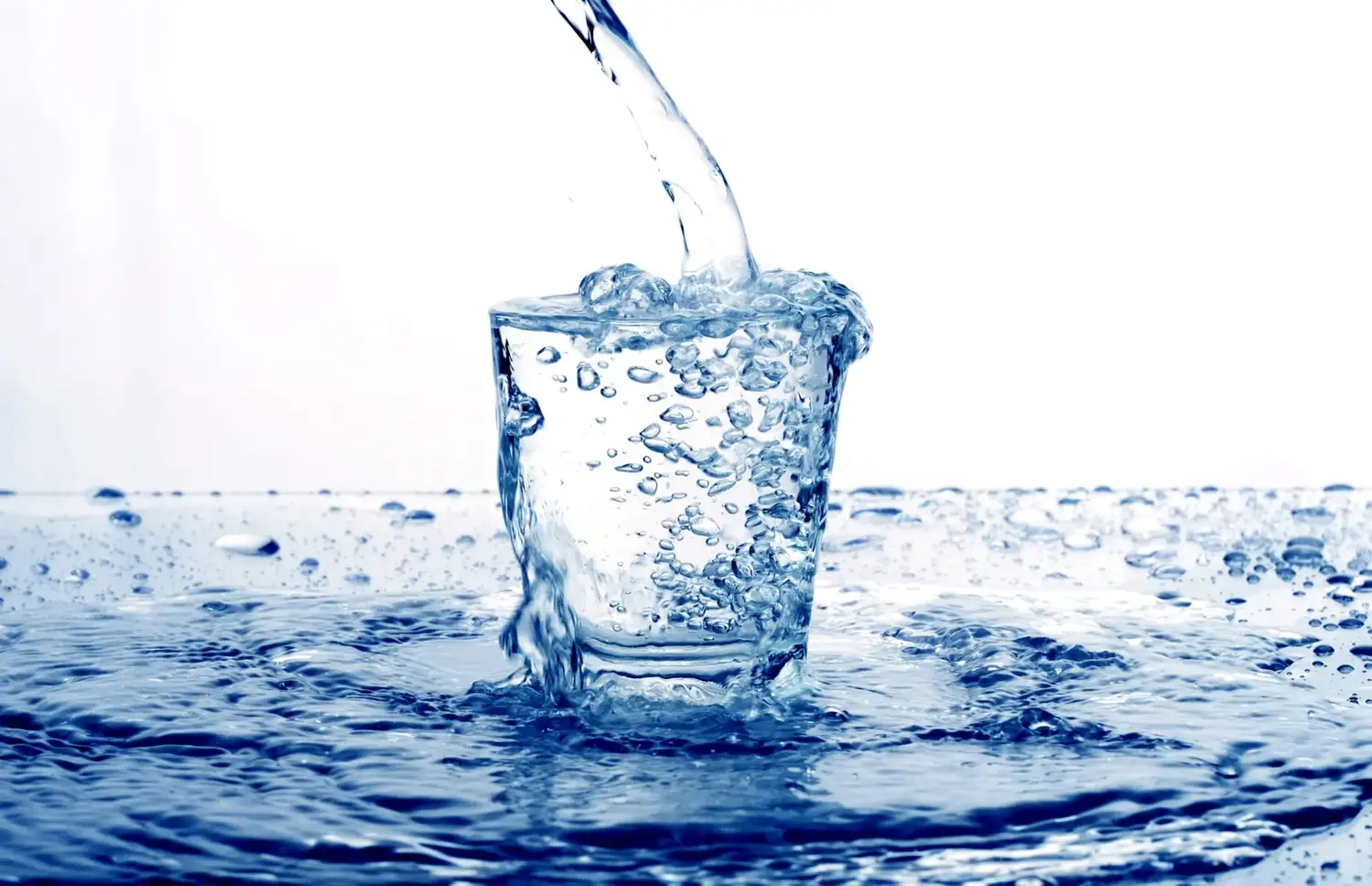Ett dricksglas överfylls av en stråle vatten där glaset står på en yta av vatten.