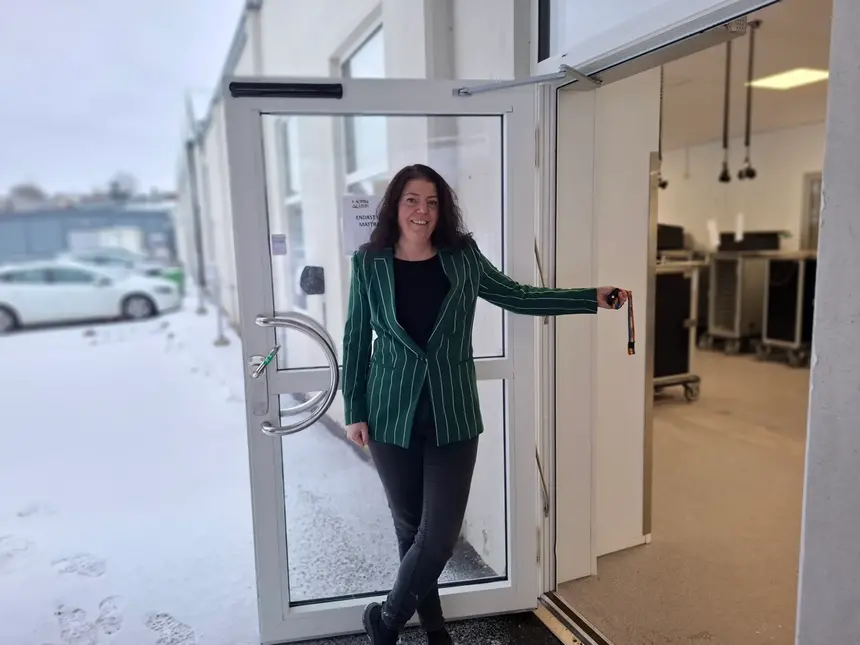 En person står i en dörröppning, bärandes en grön kavaj och jeans. En skylt med texten "LÄTT" och "ENDAST MATTE" syns till vänster.